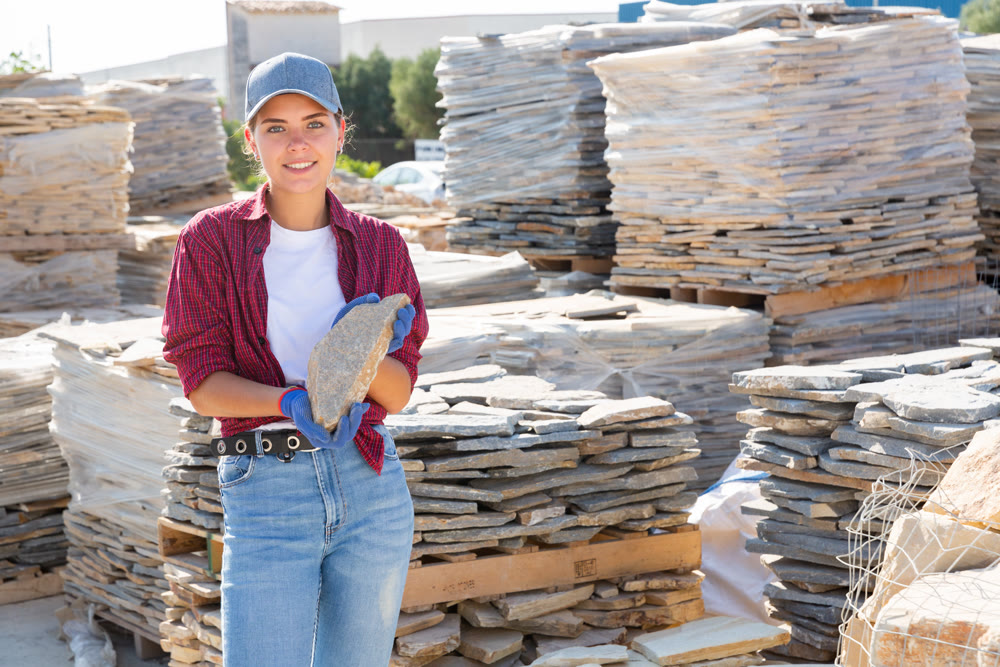 Female builder is choosing natural facing stone in the building store at an open-air construction site