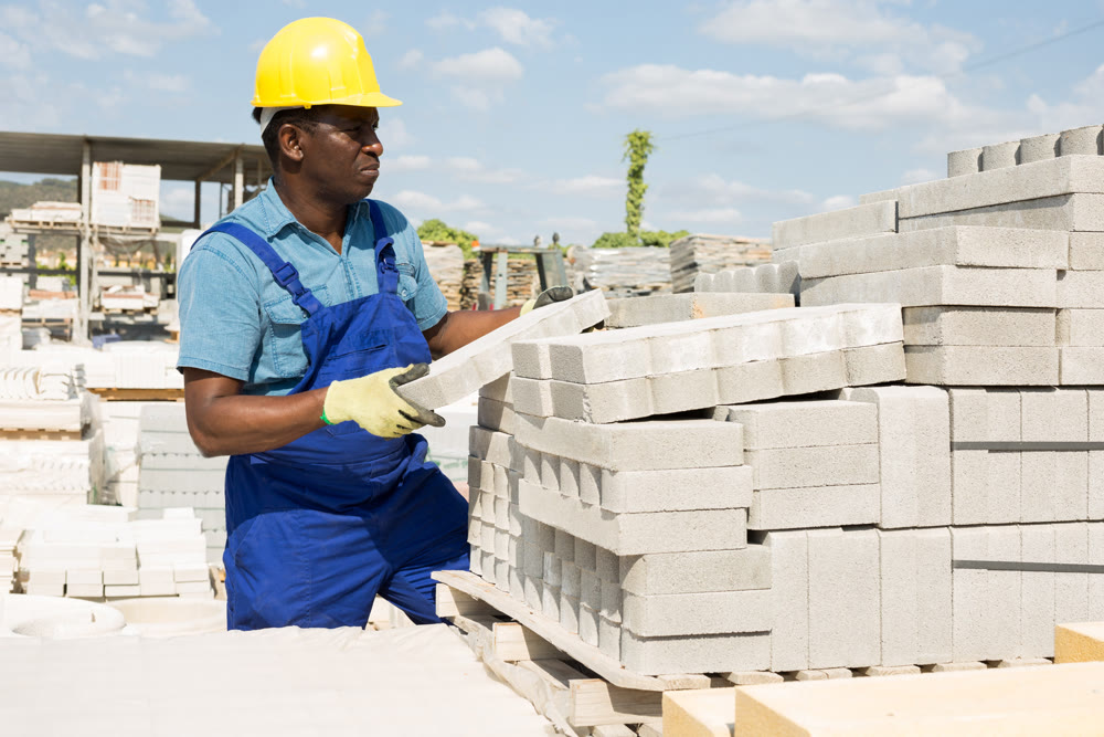 Worker stacking paving slabs in warehouse of building materials