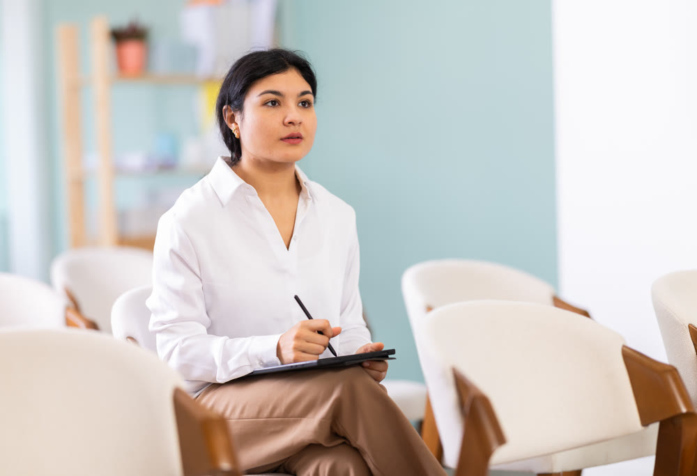 During lecture meeting, female pupil listen to teacher and write down summary in tablet