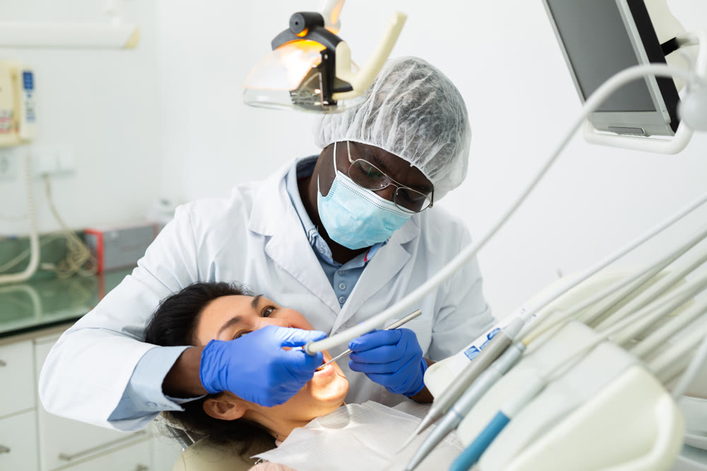 African american dentist is treating female patient which is sitting in chair