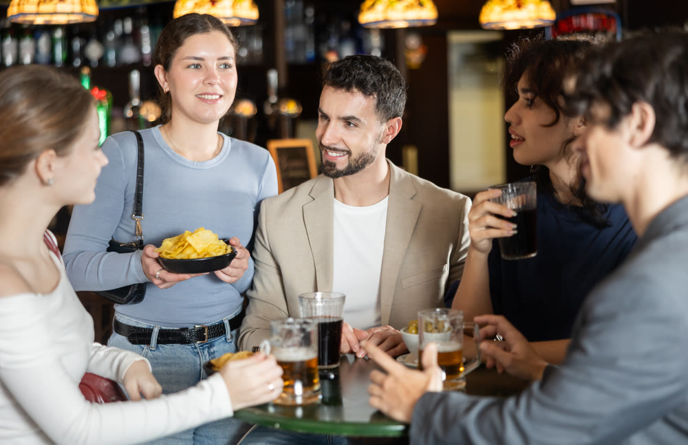 Young friends meeting at table in bar, discussion and drinking beer