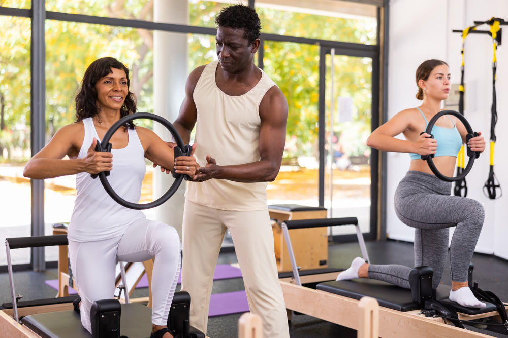 Two women having pilates workout on reformers with trainer