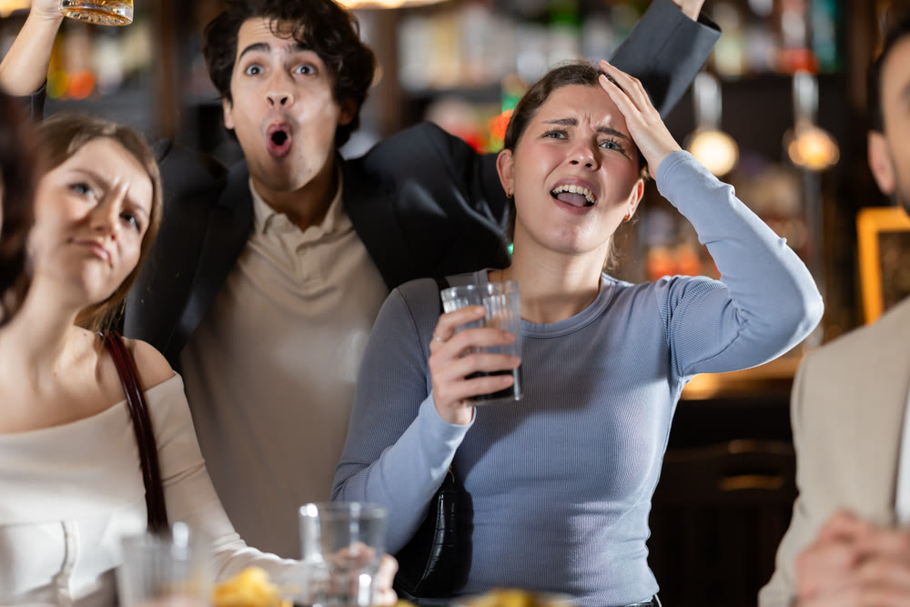 Emotional sad group of young sports fans man and woman worrying about defeat sports team, watching match on TV during rest in beer bar