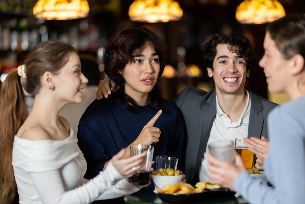 Young friends meeting at table in bar, discussion and drinking beer