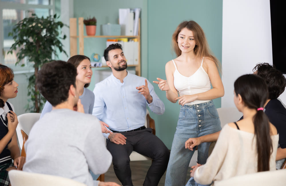 Young girl standing and talking to students sitting in a circle