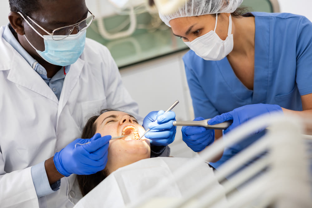 Dentist and nurse is going to treat woman patient which is sitting in dental chair