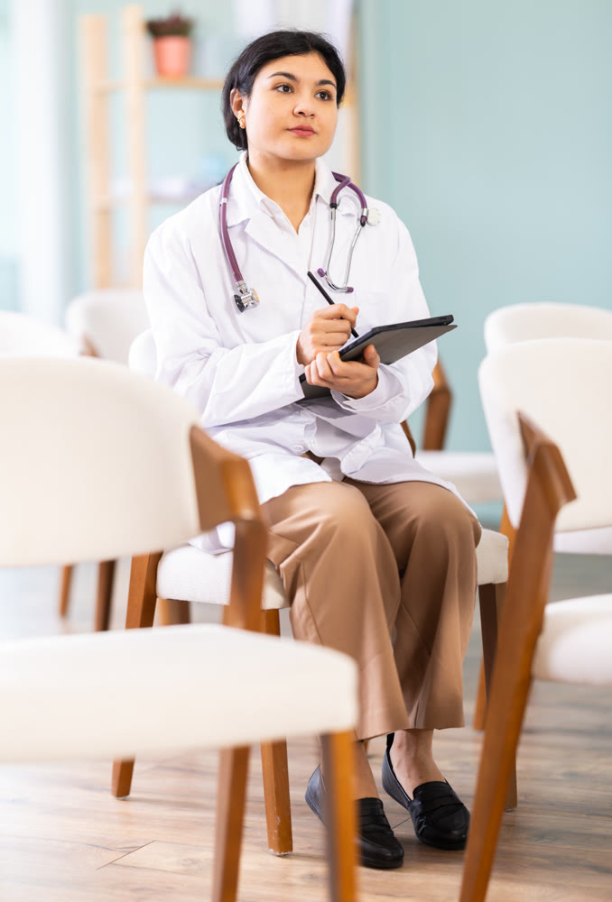 Female doctor at meeting listens to teacher and and using tablet to write down notes