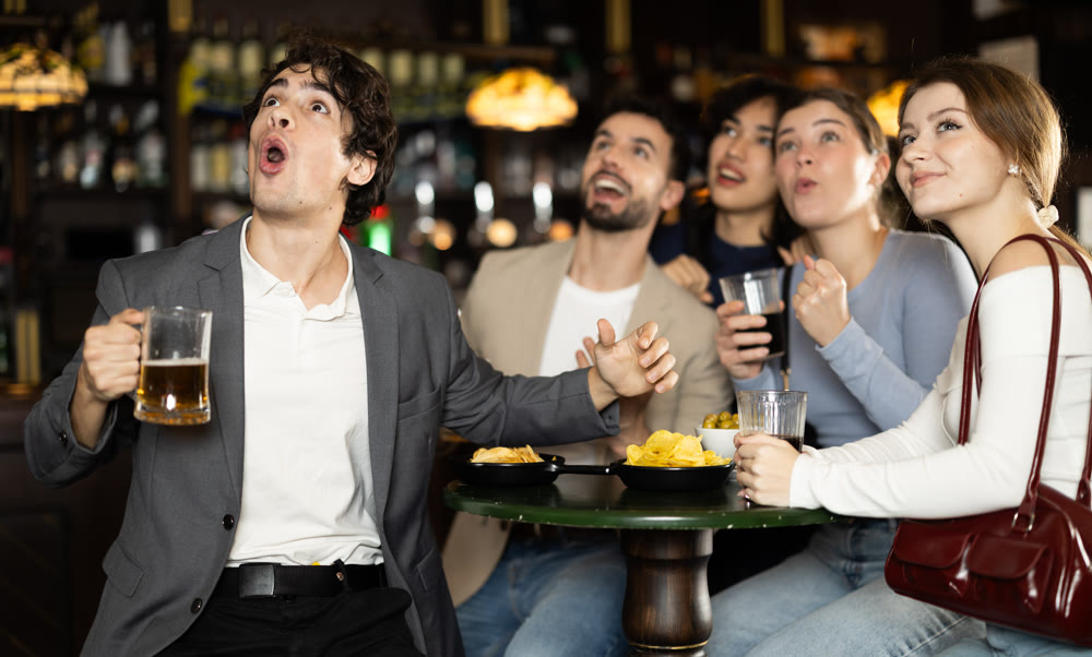 Fans watching match at a sports bar, cheering with drinks, energetic atmosphere, friendship and fun, people enjoying game together indoors