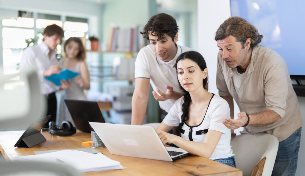 Group of coworkers gathered at one laptop and discuss working issues