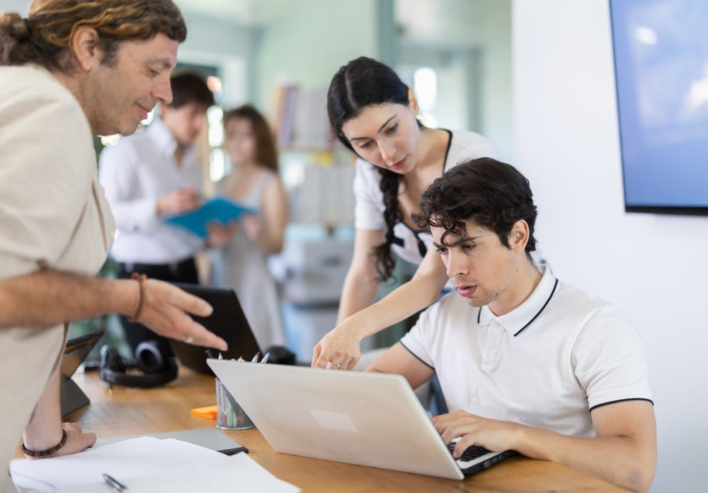 Colleagues looking at one laptop together in office