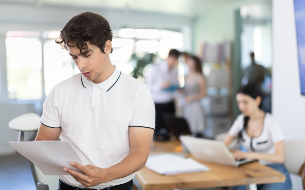 Young man standing in office holds paper documents