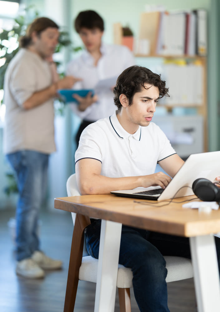 Young office worker works on laptop in modern open-plan office