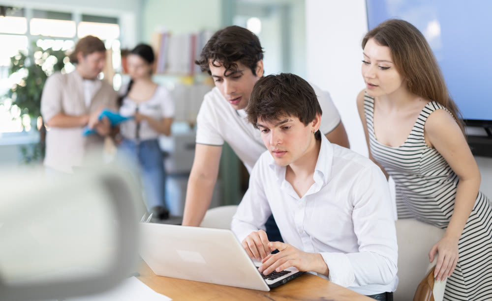 Group of coworkers gathered at one laptop and discuss working issues
