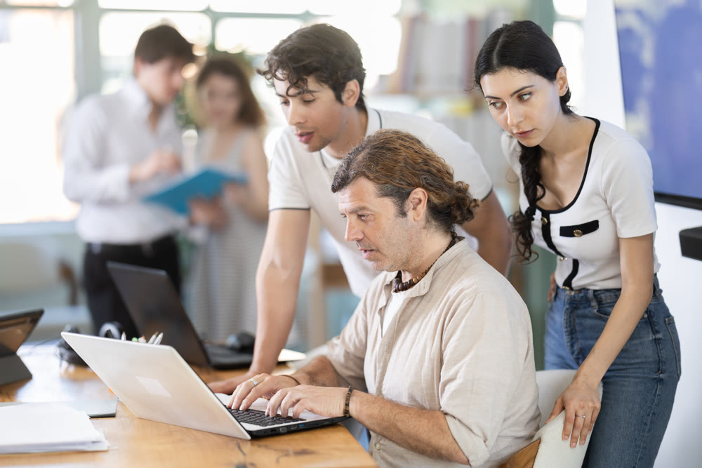 Colleagues looking at one laptop together in office