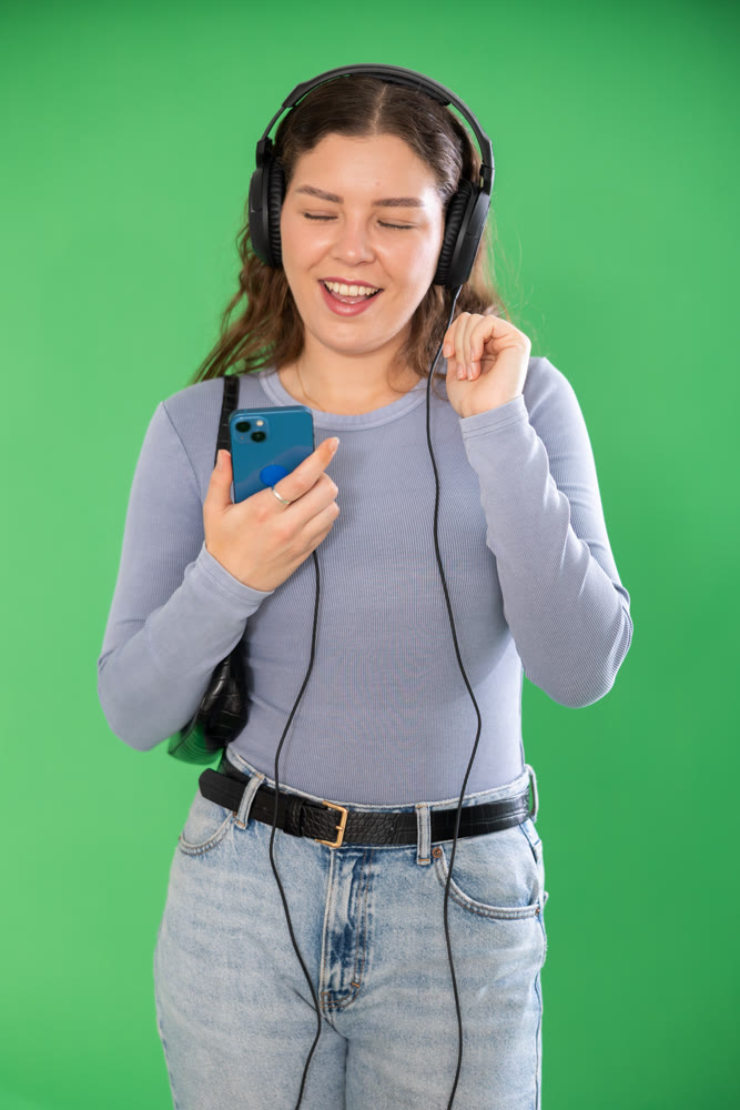 Young woman listening to music with headphones in front of green screen