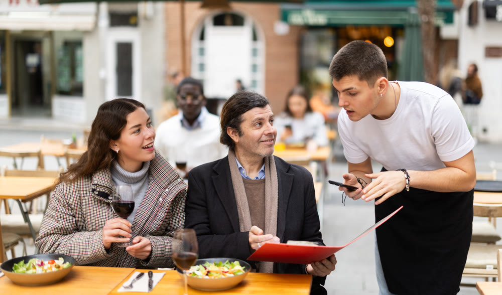 On open area of cafe, guy waiter communicates with couple of customer, accepts order
