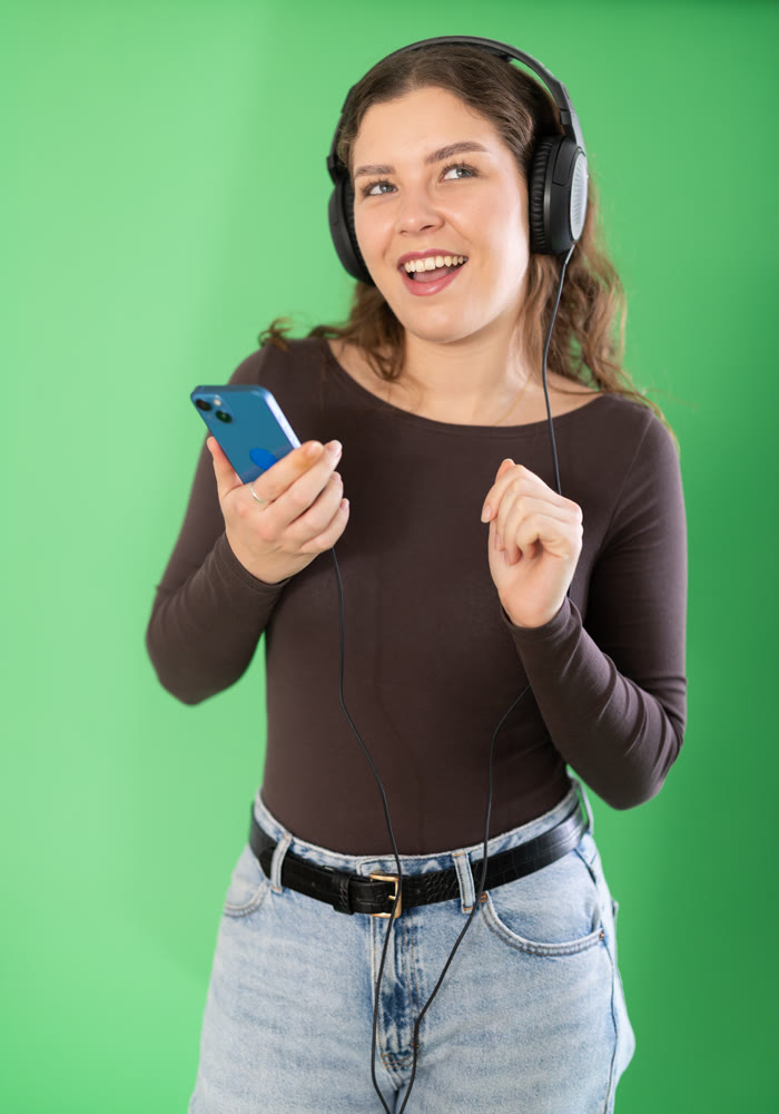 Passionate girl listening to music on headphones on green background. Chroma key compositing.