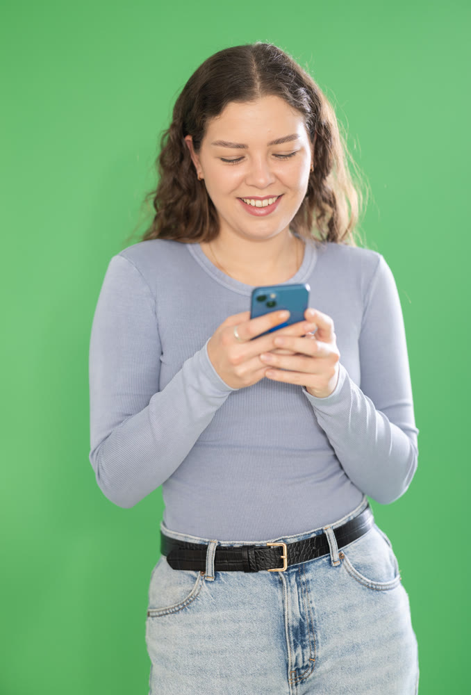 Pretty young girl scrolling through smartphone screen against green screen background. Chroma key compositing.