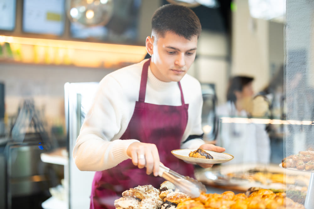 Guy salesperson and girl works in cafeteria bakery shop