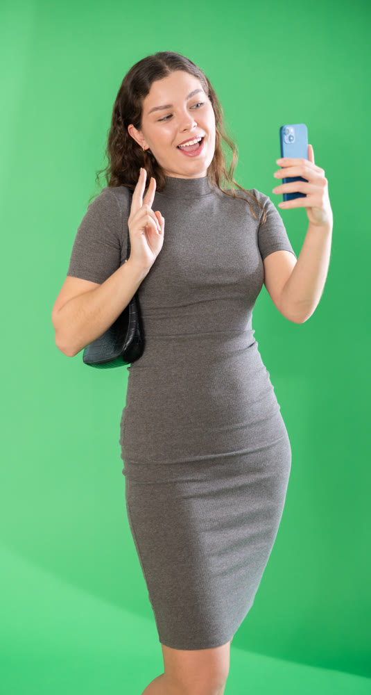 Csmiling pretty girl takes selfie on green background. Chroma key compositing.
