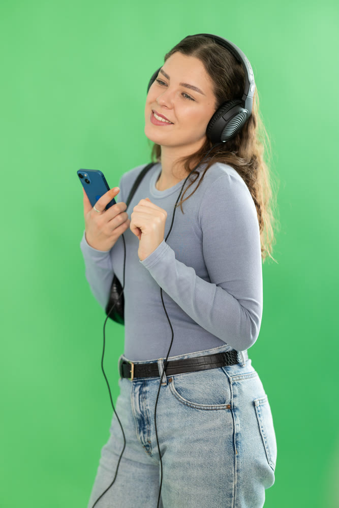Young woman listening to music with headphones in front of green screen