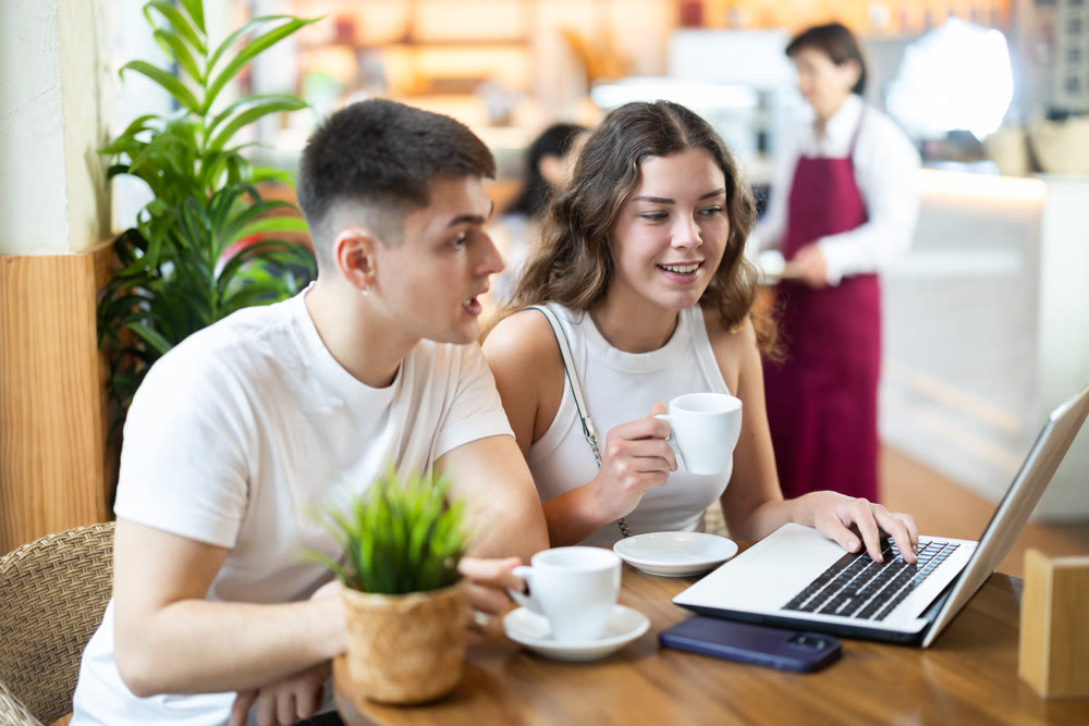 Couple man and woman with laptop drinking coffee and talking