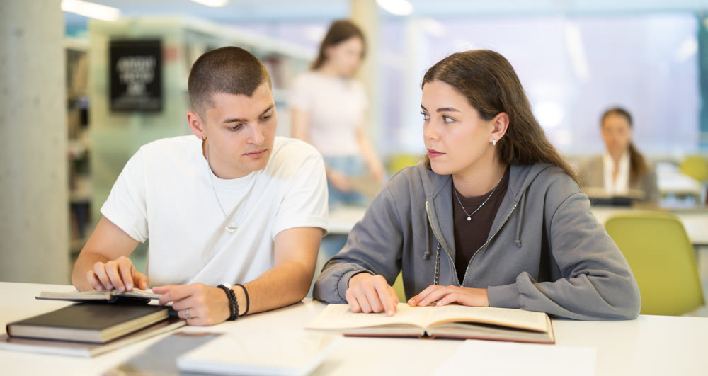 Guy and woman students reading books in library