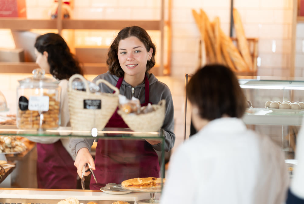 Young woman giving pastry to client in cafe