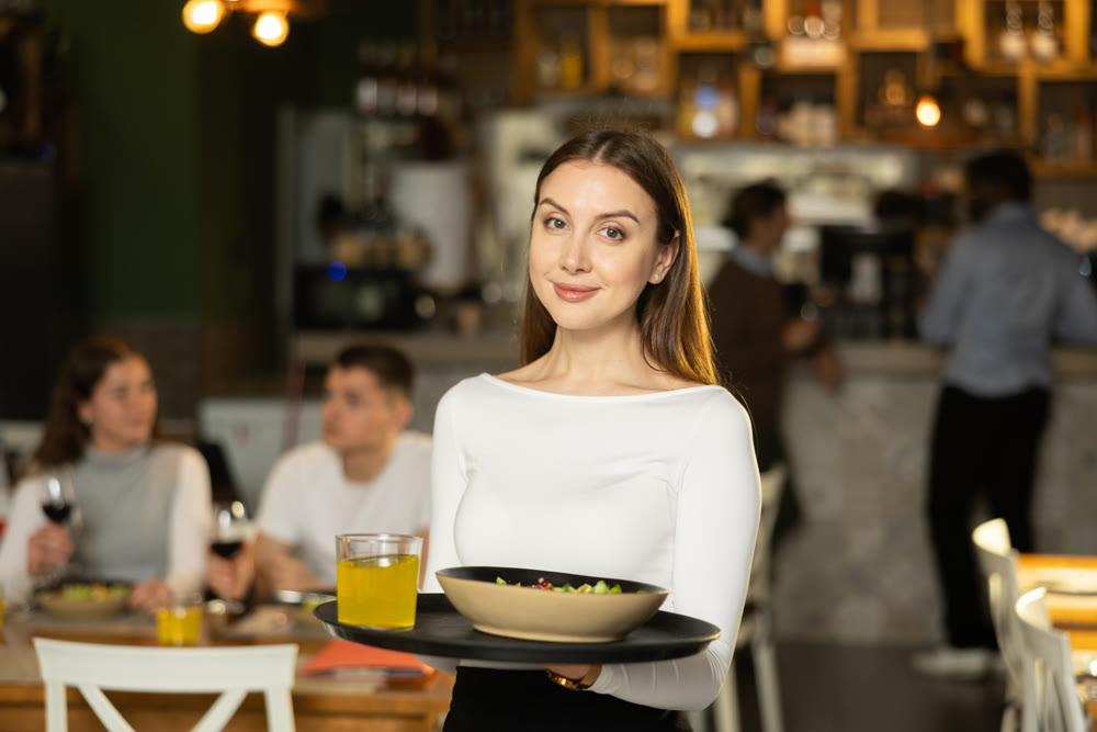 Girl of public catering cafe carries order to client, ready to serve guest of cafe establishment.