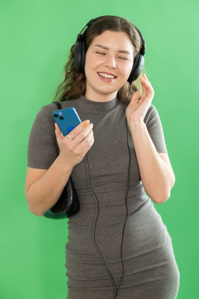 Passionate girl listening to music on headphones on green background. Chroma key compositing.
