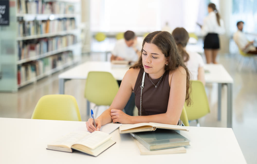 Girl reading books at table in university library - preparing for exams