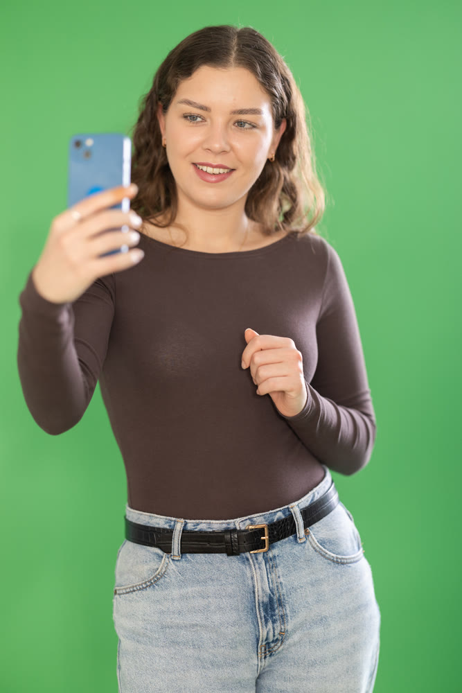 Young woman taking selfie in front of green screen