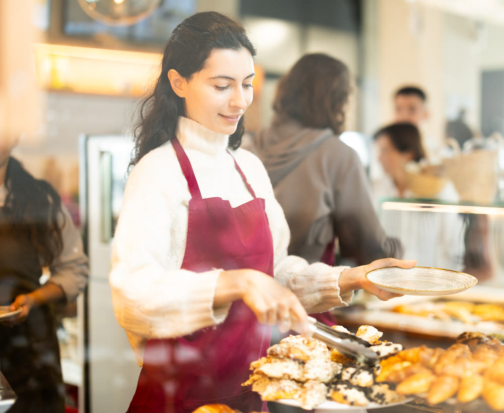 Young woman putting pastries on plate in cafe