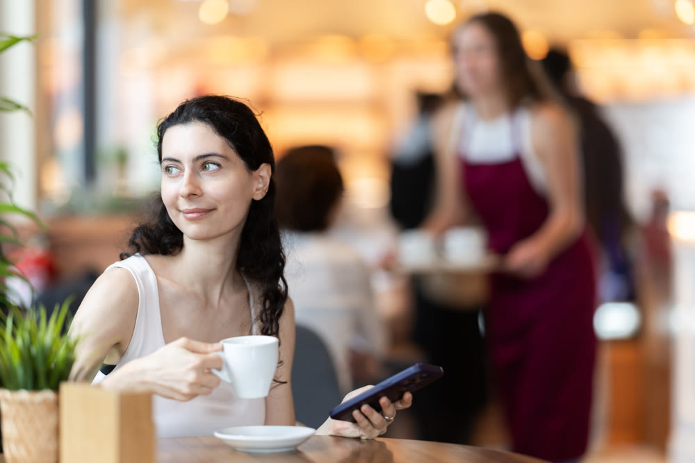 Girl in cafe drinks coffee and calling using mobile phone