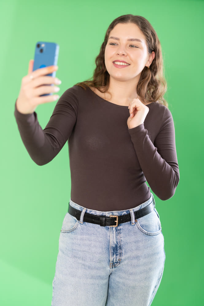Young woman taking selfie in front of green screen