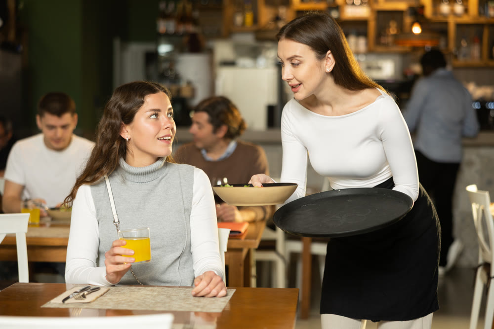 Girl waitress serves cafe establishments girl visitor, puts food on table.