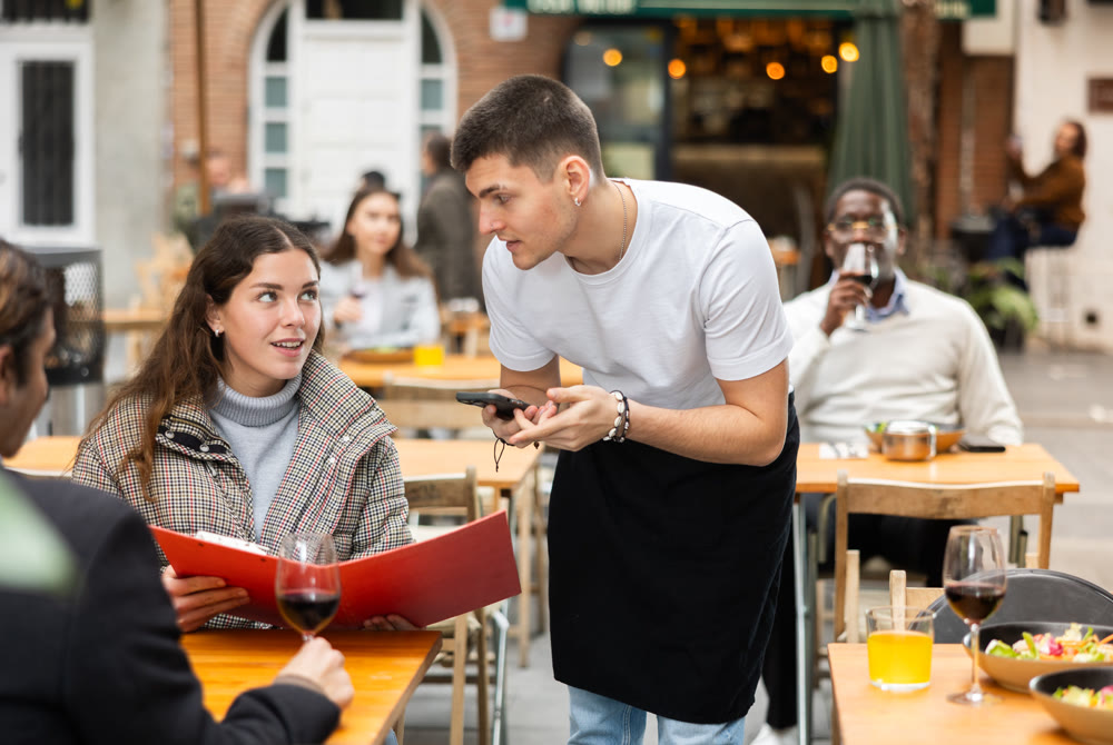 On open area of cafe, guy waiter communicates with girl customer, accepts order