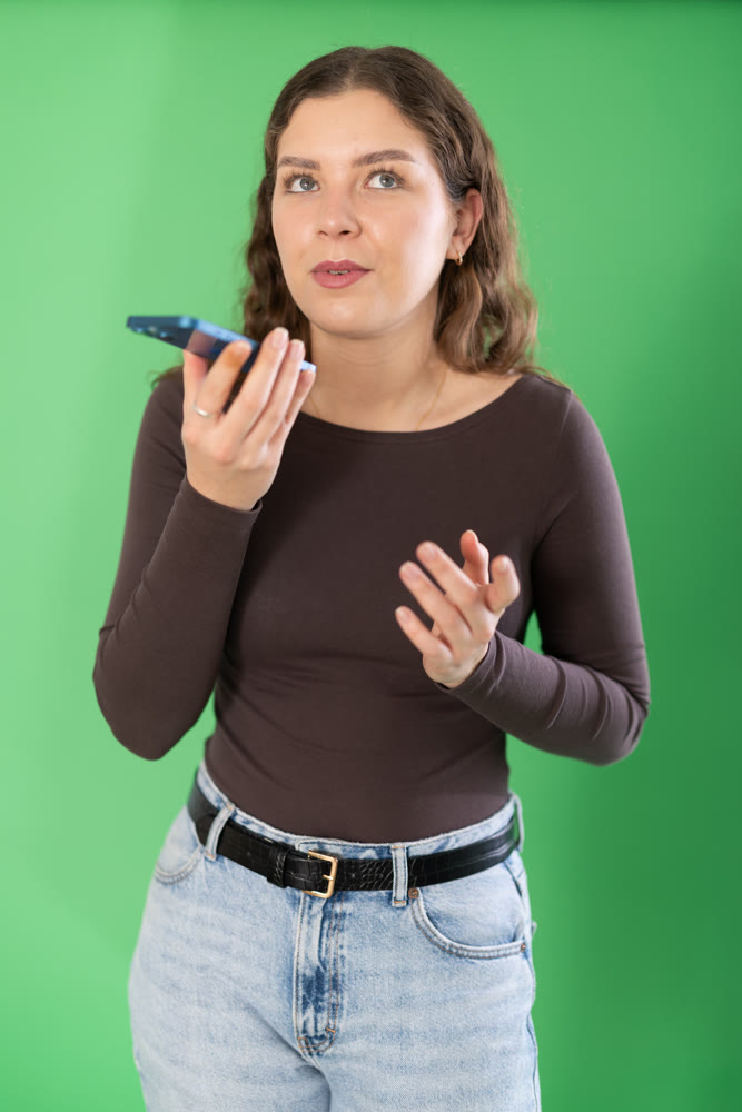 Young woman recording voice message in front of green screen