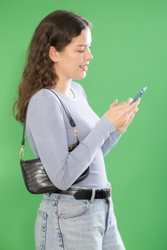 Young woman scrolling smartphone screen in front of green screen