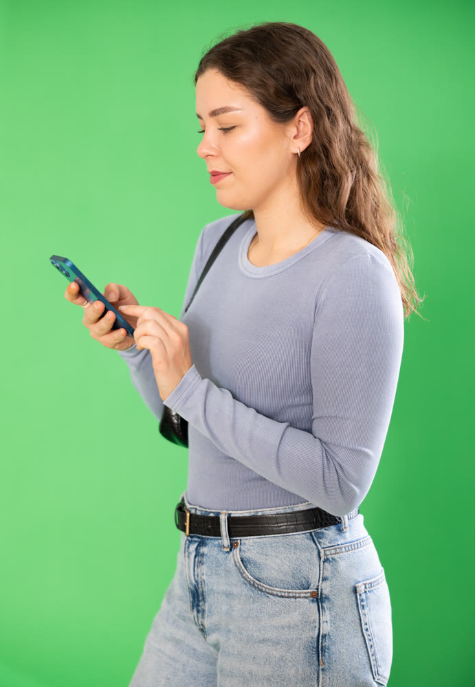 Pretty young girl scrolling through smartphone screen against green screen background. Chroma key compositing.