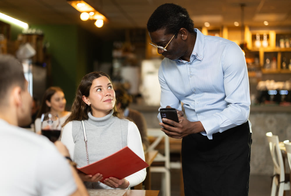 Woman, after reading the menu, makes an order from an African waiter