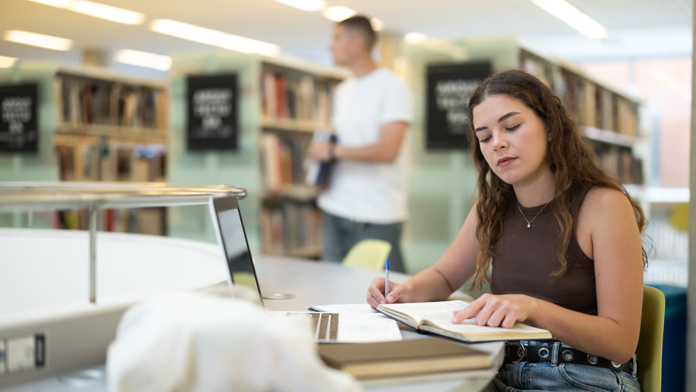 Female student reading books and working on laptop