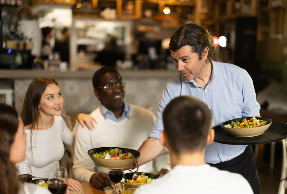 Man waiter serves cafe establishments couple visitor, puts food on table.