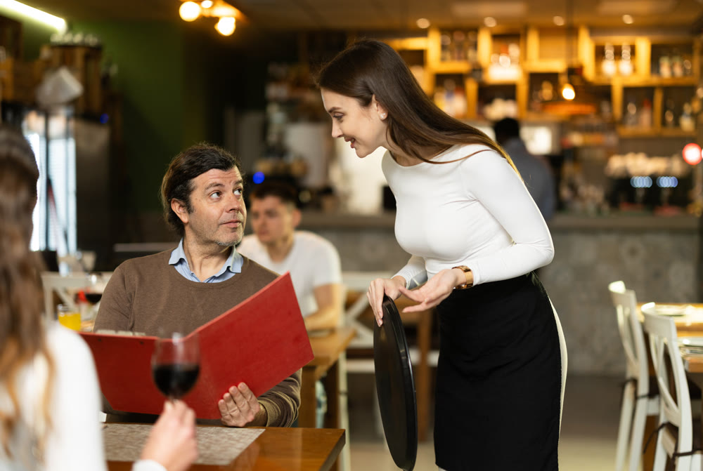 Man, after reading the menu, makes an order from the waitress