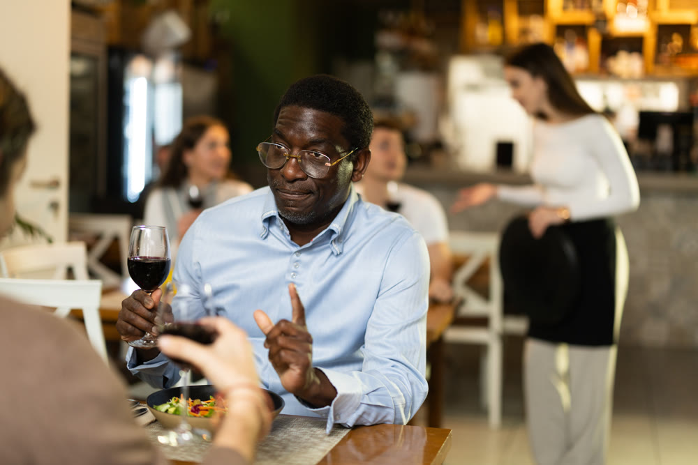 African man in cafe sits opposite male companion, has nice conversation