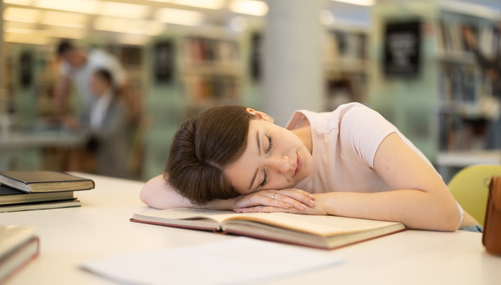 Female student tired and lay down on table in library