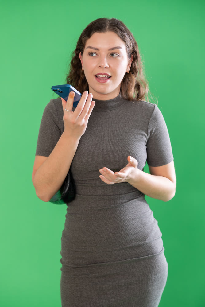 Young woman recording voice message in front of green screen