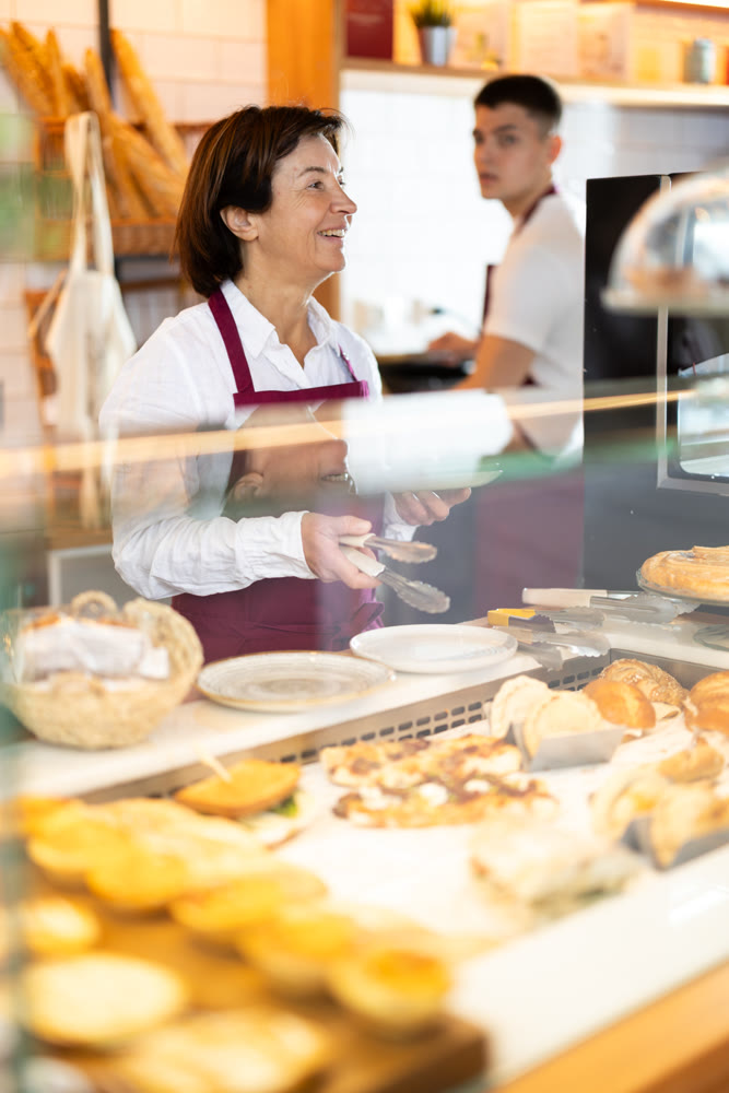 Elderly woman puts pastries on plate in cafe