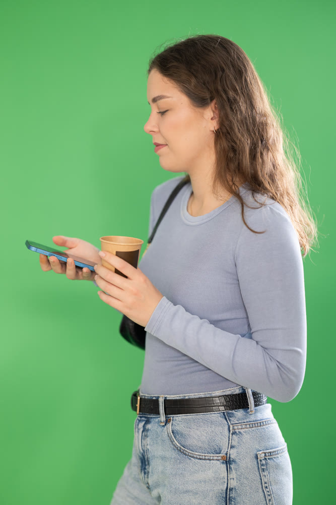 Girl with cup of coffee scrolls phone screen or types text message