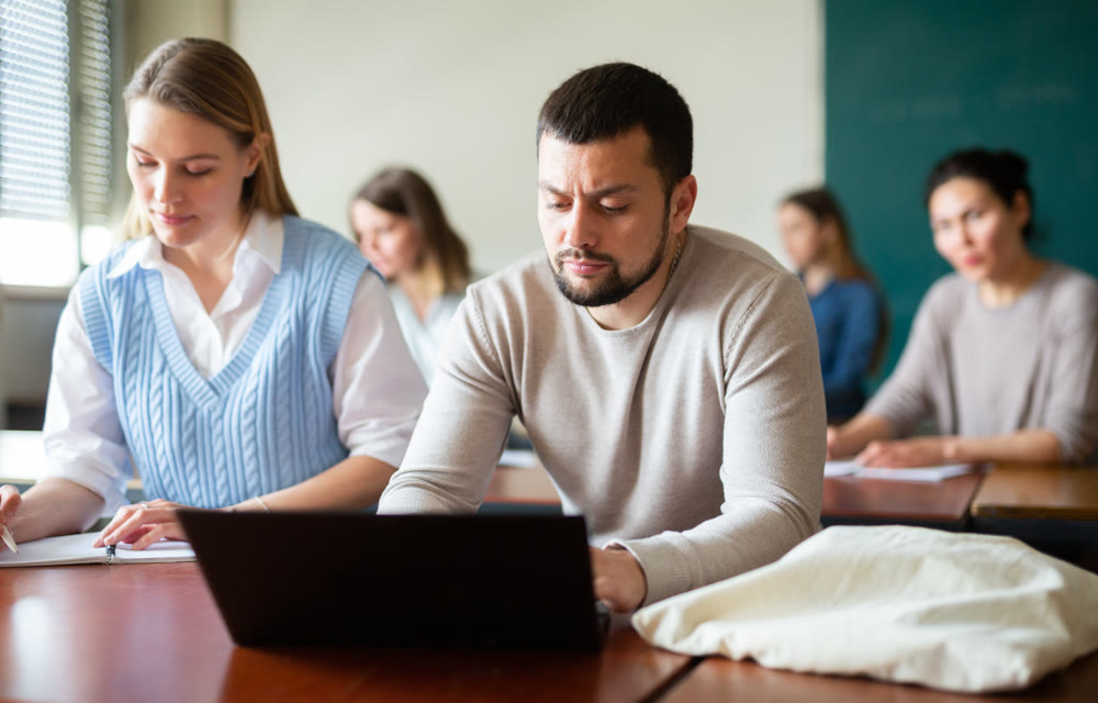 Handsome male student typing on laptop during lecture at university